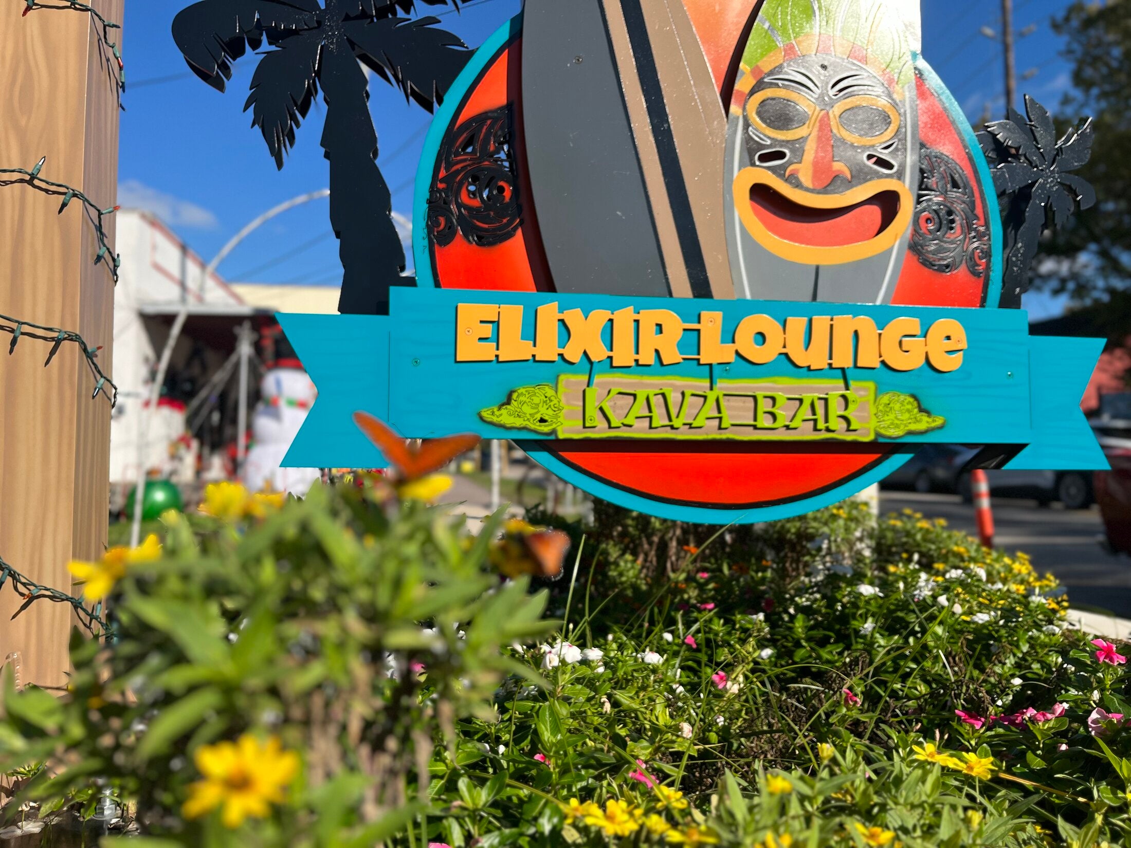 Colorful Elixir Lounge Kava Bar tiki sign above a flower bed with a butterfly in Old Town Spring.