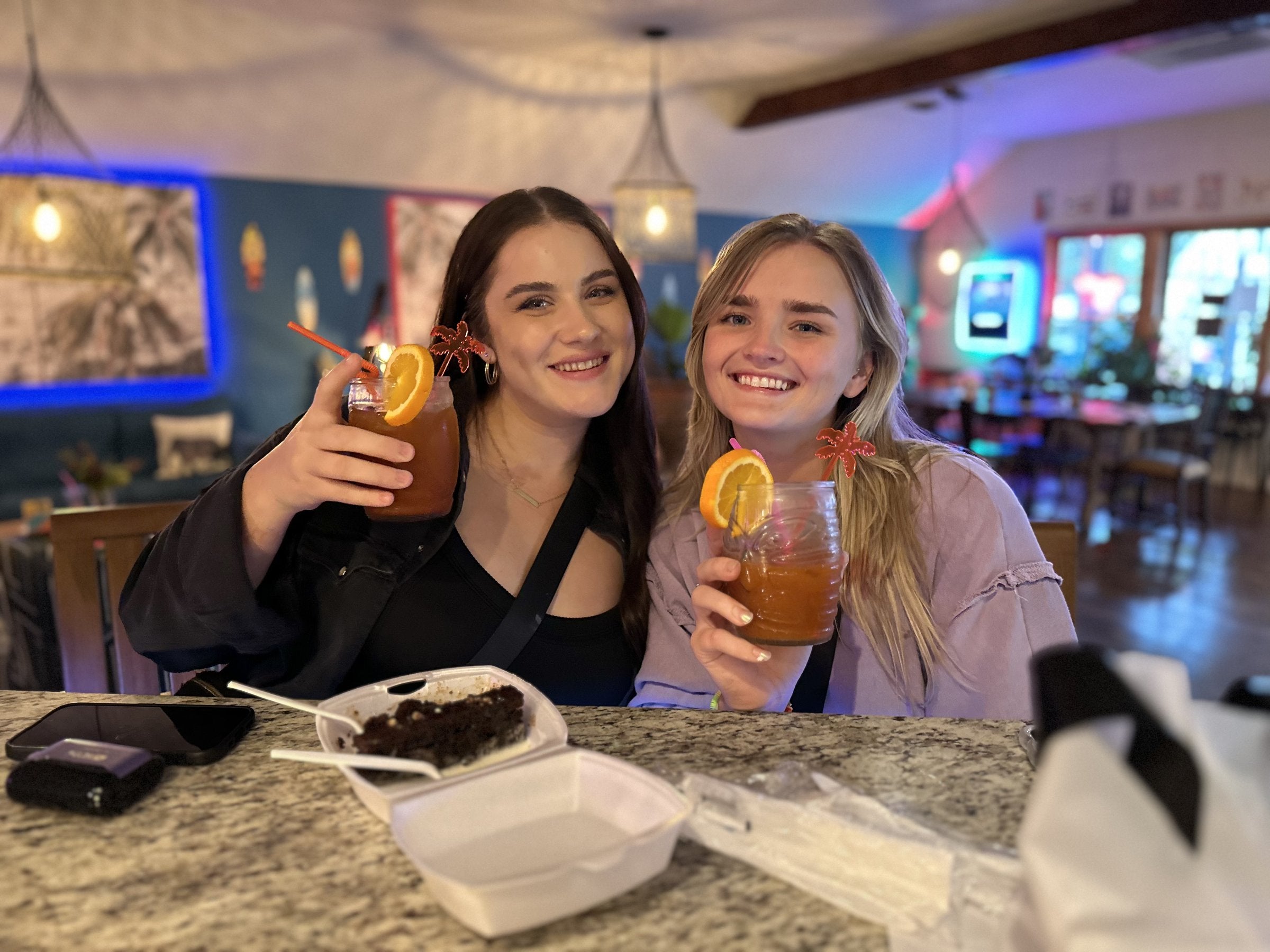Two friends smiling with garnished tiki drinks at the Elixir Lounge bar