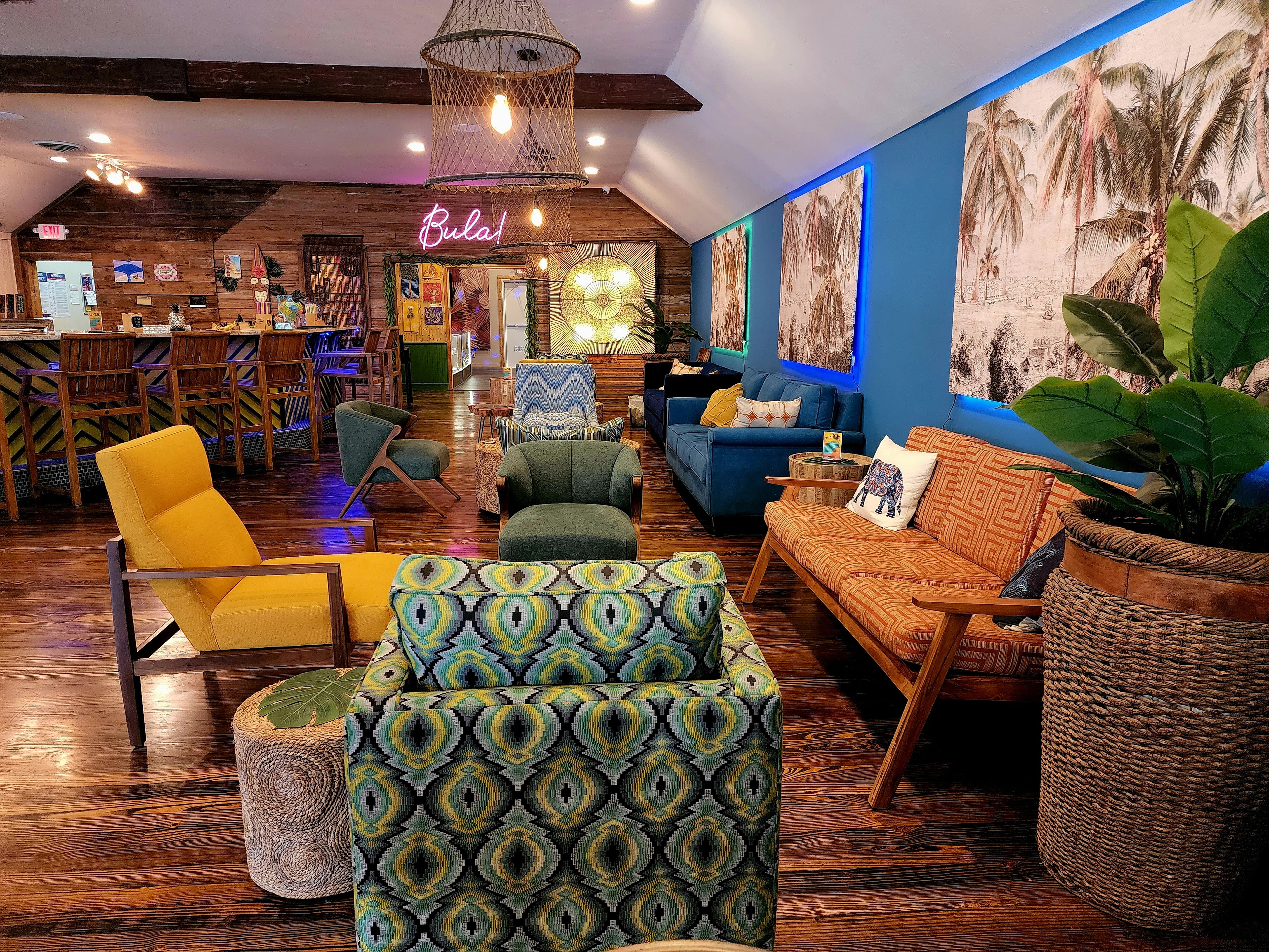Wide view of the Elixir Lounge main room with tiki bar, palm murals, Bula neon and colorful lounge seating.