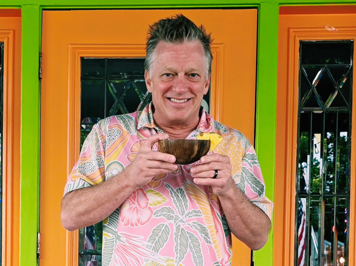 Smiling Elixir Lounge owner holding a coconut kava bowl with pineapple at the colorful storefront doors.